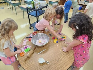Four female students in Grade One play with homemade playdough at a round table in a classroom.