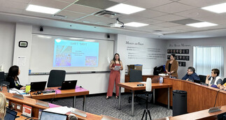 Female student at the front of a board room makes a presentation to Chinook Board of Education members and senior admin staff.